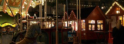 Ein Kinderkarussel auf einem Weihnachtsmarkt mit roten Häuschen vor dem Düsseldorfer Rathaus.