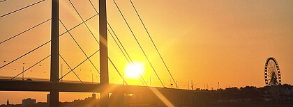 Ein oranger Sonnenuntergang hinter der Rheinkniebrüke mit dem Riesenrad für die Rheinkirmes