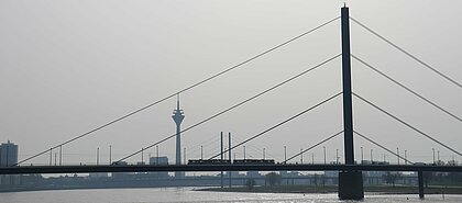 Auf dem Bild sieht man die Rheinkniebrücke und den Fernsehturm in Düsseldorf. Über die Brücke fährt eine Ubahn.