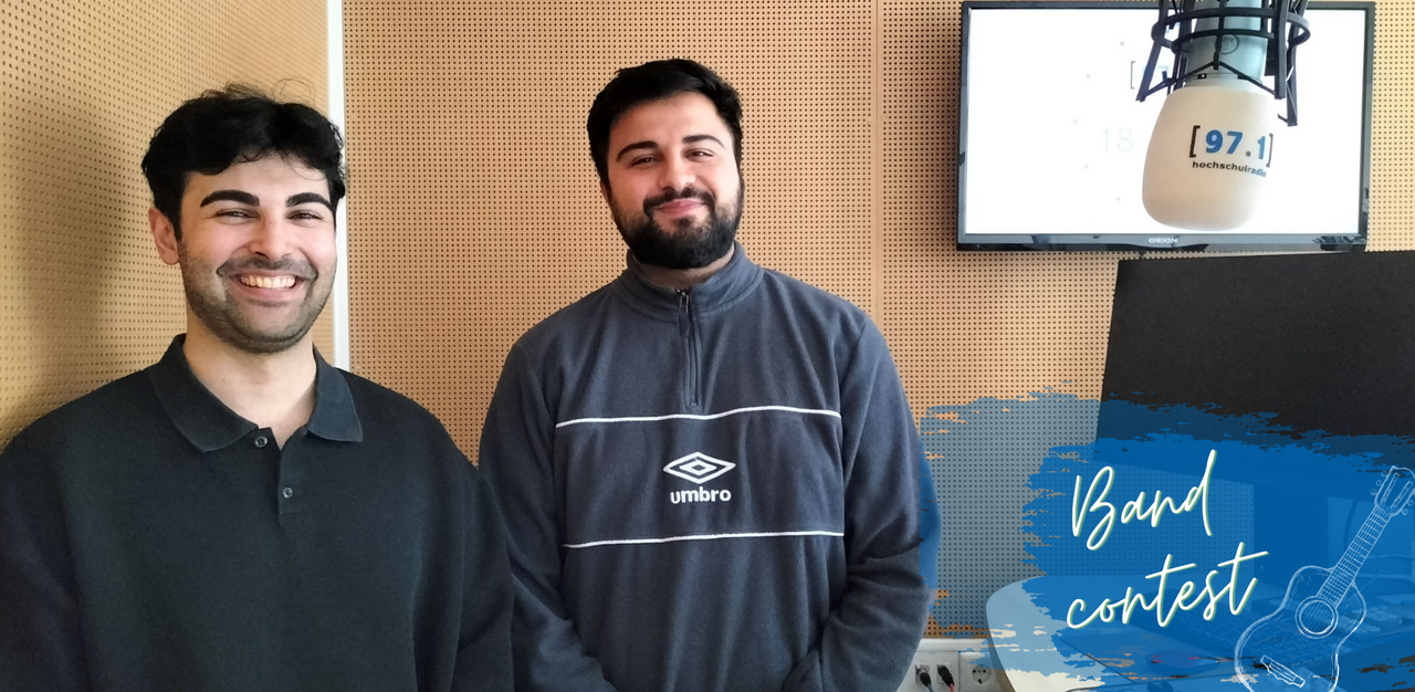 Auf dem Bild sieht man zwei Mitglieder der Band Safespace Society. Sie lächeln in die Kamera und stehen im Studio von hochschulradio düsseldorf. Ganz rechts befindet sich ein weißes Mikrofon mit dem Logo von hochschulradio düsseldorf (Foto: Johanna Warszawa)