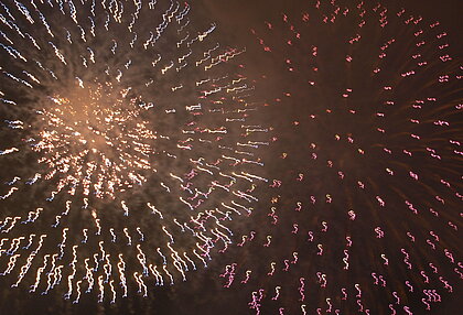 Auf dem Bild sieht man am dunklen Nachthimmel explodierenden Feuerwerkskörper