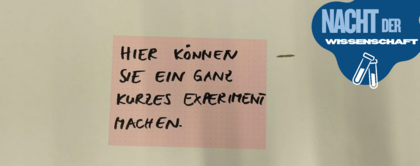 Auf dem Bild ist ein Zettel zu sehen. Auf dem Zettel steht „Hier können Sie ein ganz kleines Experiment machen“.