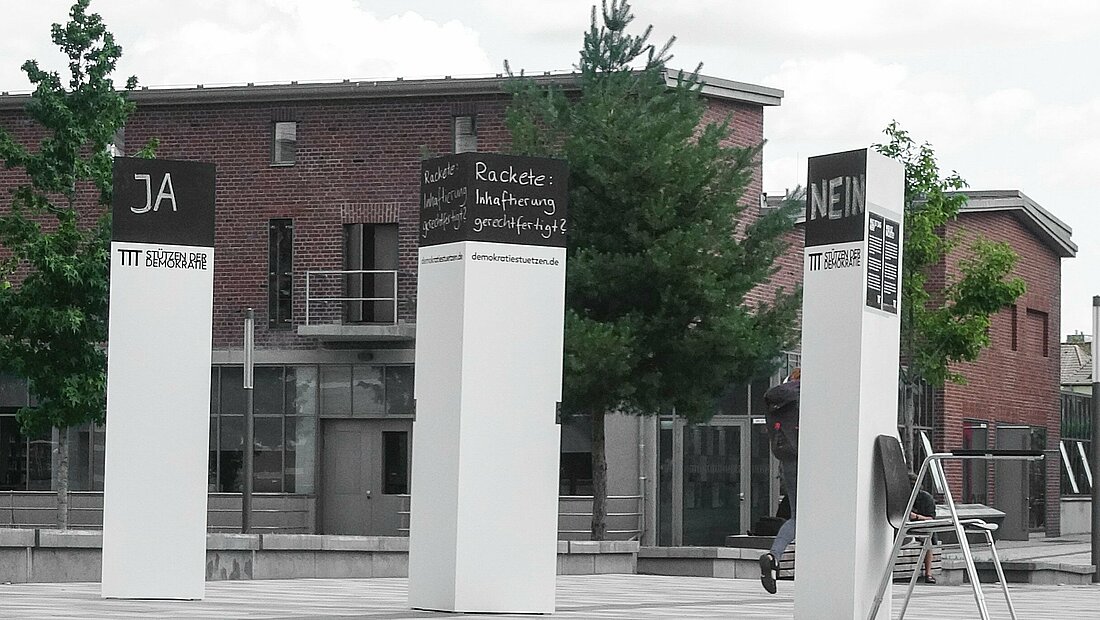 Man sieht drei Säulen an der Hochschule Düsseldorf. In der Mitte steht eine Entschiedungsfrage, die anderen beiden Säulen dienen als Antwortmöglichkeit. 