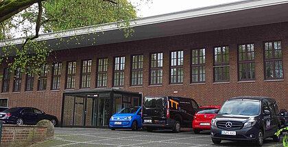 Auf dem Foto it das ZDM zu sehen. Es ist ein längliches Backsteingebäude vor dem Autos stehen.